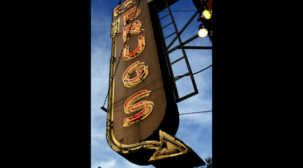Neon drugstore sign saying "Drugs" with an arrow